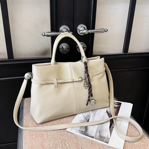 Sac cabas en cuir grainé crème avec breloque florale et bandoulière sur socle en pierre