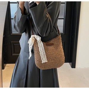 Detail of hand-woven straw bucket bag with white lace trim and brown leather strap