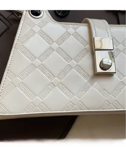 Close-up of ivory shoulder bag featuring geometric embossed pattern and silver twist lock
