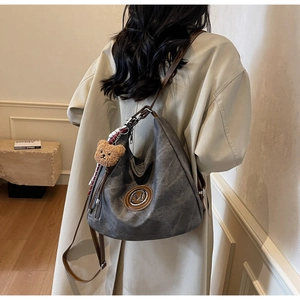 Dettaglio della borsa hobo grigia con logo M in metallo e ciondolo a orsetto
