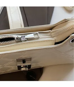 Close-up of silver metal zipper and hardware on cream textured leather shoulder bag