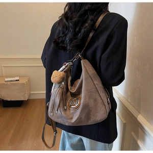 Dettaglio borsa hobo marrone vintage con logo M, cerniera a frange e ciondolo orso