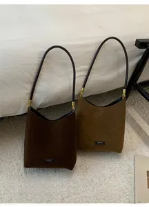 Detail of suede bucket bags in brown and olive green with leather straps and gold hardware