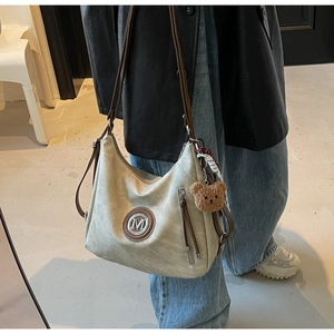 Dettaglio borsa tote beige con logo M, pendente orso e sciarpa su persona in blazer