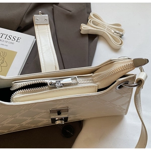 Detail of cream shoulder bag featuring geometric embossed texture and silver metal clasp