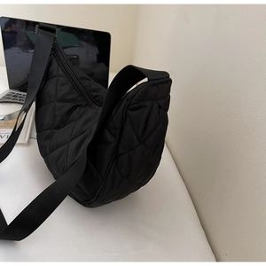 Dettaglio macro della borsa a mezzaluna in nylon trapuntato nero su scrivania bianca