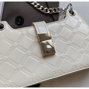 Detail of cream shoulder bag featuring geometric embossed leather and silver chain strap