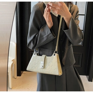 Detail showing the geometric G-embossed pattern and silver buckle on a cream shoulder bag