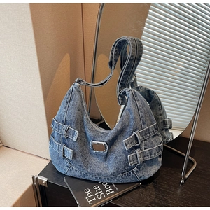 Détail du sac hobo en denim bleu avec sangles latérales réglables et plaque logo métallique
