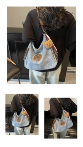 Dettaglio della borsa hobo azzurra con finiture in pelle marrone e ciondolo a orsetto