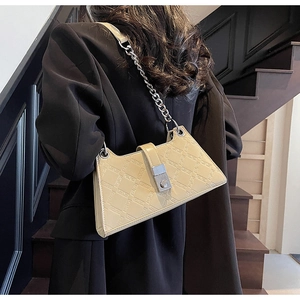 Detail of beige underarm bag with geometric embossing and chain strap on a model