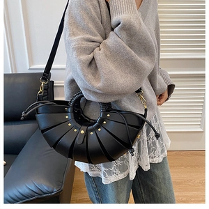 Détail d'un sac demi-lune noir avec plis éventail, clous dorés et poignée tressée