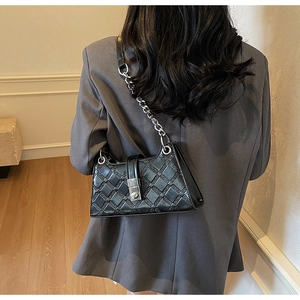 Rear view of model wearing a black quilted leather underarm bag with silver chain strap