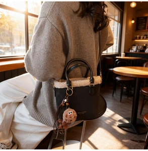 Détail du sac seau en cuir noir avec bordure en molleton blanc et breloque petit bonhomme