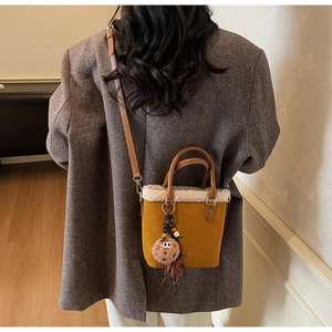 Détail du sac seau moutarde avec bordure en peau lainée, poignée en cuir et breloque