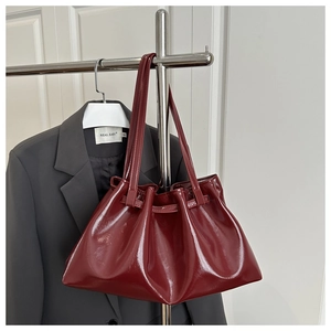 Detail of burgundy glossy tote bag with pleated texture styled on a grey suit jacket