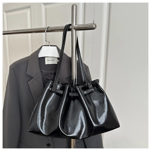 Detail of black pleated tote bag in glossy faux leather hanging on a stainless steel rack