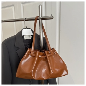 Detail of glossy brown pleated tote bag with thin straps on a metal display stand