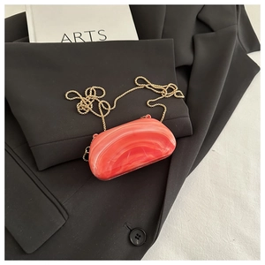 Detail of orange marble acrylic clutch bag with gold bead chain on black blazer