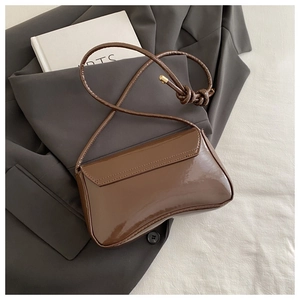 Detailed close-up of brown patent leather texture and knotted strap on underarm bag