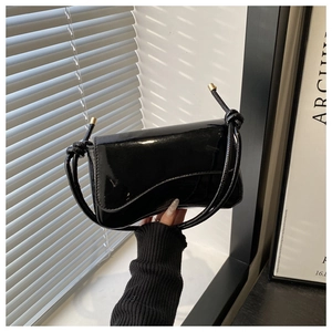 Detail of glossy black patent leather underarm bag with unique knotted strap and metal caps