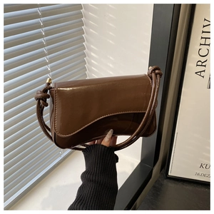 Close-up of brown glossy leather shoulder bag with irregular flap and knot strap detail