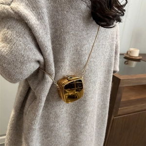 Mini gold acrylic box bag with metallic chain strap worn over a grey knit sweater