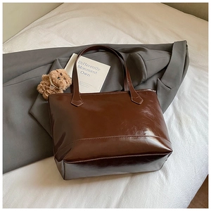 Detail of dark brown glossy tote bag with leather texture and bear plush charm accessory