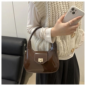 Detail of glossy brown patent leather crescent bag with golden metal buckle on a model