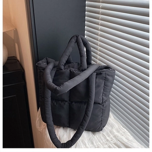 Close-up of black quilted puffer tote bag with puffy padded texture on lace fabric