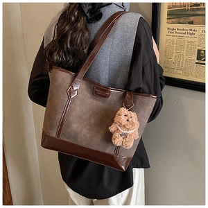 Detailed view of dark brown tote bag featuring vintage pattern and a cute teddy bear charm