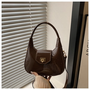 Detailed close-up of dark brown patent leather crescent bag with gold metal clasp