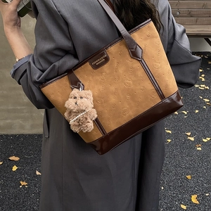 Retro brown embossed tote bag with cat pattern and cute plush bear charm on a model's shoulder
