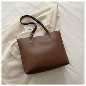 Brown leather tote bag with long shoulder strap displayed in a chic office setting