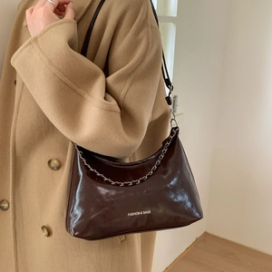 Détail d'un sac demi-lune marron brillant avec chaîne argentée porté sur un manteau