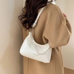 Détail d'un sac demi-lune blanc avec chaîne en argent sur un manteau beige