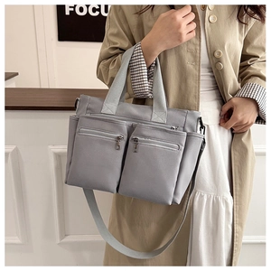 Detailed view of grey nylon tote bag with functional zippers and woven top handles