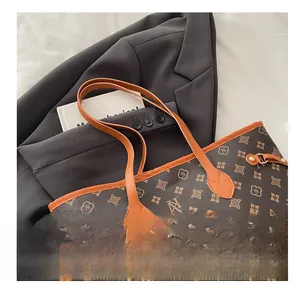 Detail of monogram tote bag with orange handles and gold hardware on black suit background