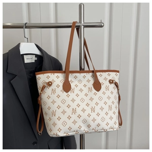 Detail of classic tote bag with monogram print and brown leather handles hanging on stand