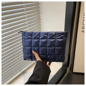 Detail of navy quilted puffer clutch bag with metallic sheen and zipper closure