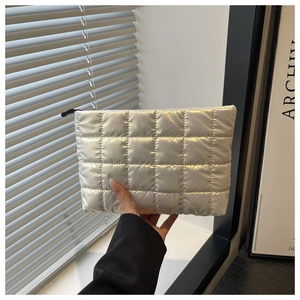 Silver quilted cosmetic bag held by hand, featuring metallic finish and top zipper detail