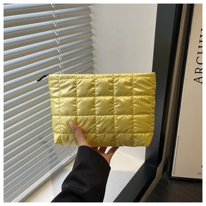 Close-up of a bright yellow quilted nylon clutch bag with black zipper and square stitching