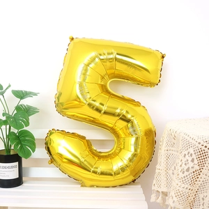 Golden number 5 foil balloon on a white bench with monstera plant for birthday party decor