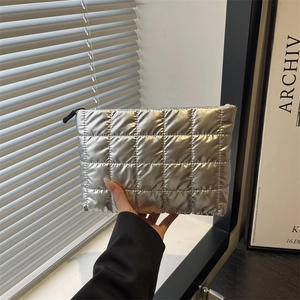 Chic silver metallic quilted cosmetic bag with zipper closure held by hand in a trendy room