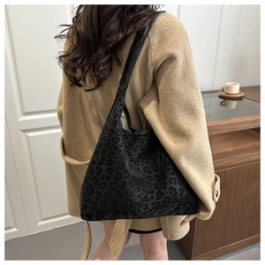 Detail of minimalist black leopard print hobo bag worn with a camel winter coat