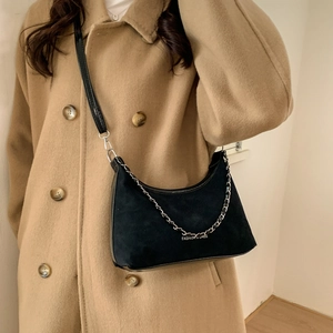 Détail d'un sac bandoulière noir mat avec chaîne en argent porté sur un manteau brun