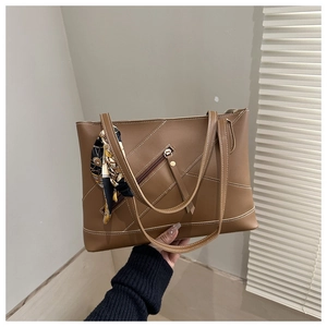 Detailed view of brown leather tote bag with contrast stitching and silk scarf wrap handle