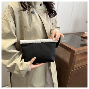 Dettaglio della pochette in camoscio nero con bordo in shearling bianco tenuta da una modella