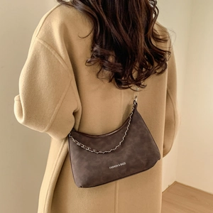Sac bandoulière rétro en daim marron foncé avec chaîne argentée porté sur manteau