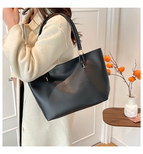 Detail of minimalist black leather tote bag with gold metal buckle and long handle